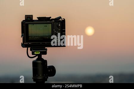 Una fotocamera professionale su un treppiede si affaccia su un tramonto tranquillo, pronto a catturare il momento perfetto. Foto Stock