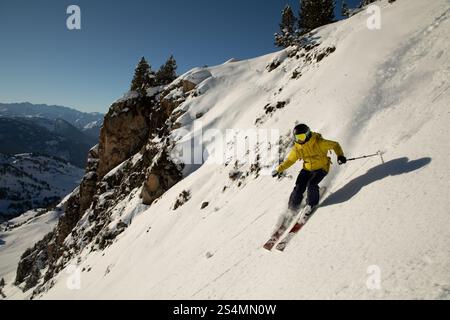 Un'immagine emozionante di uno sciatore che scivola giù da una ripida e innevata pendenza di montagna sotto la luce del sole la posa dinamica dello sciatore e l'attrezzatura vibrante creano un'eccitazione Foto Stock