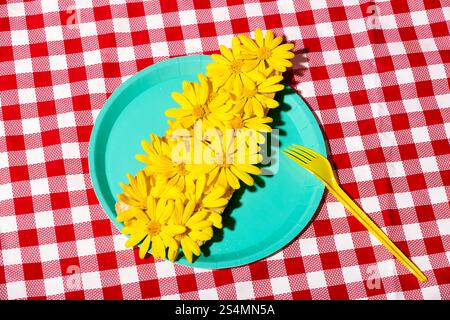 Una disposizione visivamente sorprendente di fiori gialli freschi su un piatto turchese vibrante adagiato su una tovaglia a scacchi rossa. Perfetto per temi di somma Foto Stock
