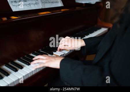 Un primo piano delle mani di un pianista che suona con grazia un pianoforte a coda, sottolineando l'eleganza e l'abilità nella performance musicale Spartiti musicali si trova in cima alla Foto Stock