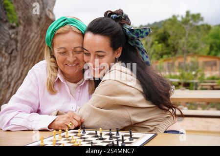 Un momento toccante mentre madre e figlia si divertono a giocare a scacchi all'aperto il loro legame e i loro sorrisi riflettono gioia e connessione in un ambiente sereno e naturale Foto Stock