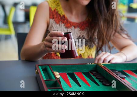 Una donna viene catturata a metà partita, lanciando dadi mentre gioca a backgammon a un tavolo, il vivace tabellone aggiunge emozioni e concentrazione alla scena Foto Stock