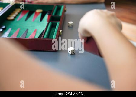 Una mano lancia i dadi accanto a un tabellone di backgammon, mettendo in evidenza gli elementi strategici e l'emozione del gioco, il tabellone colorato e i dadi creano un vibr Foto Stock