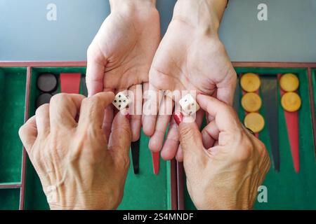 Primo piano di mani che tengono i dadi su un tabellone di backgammon, catturando l'attesa prima di un lancio, i colori vivaci del tabellone mettono in risalto questo classico gam Foto Stock