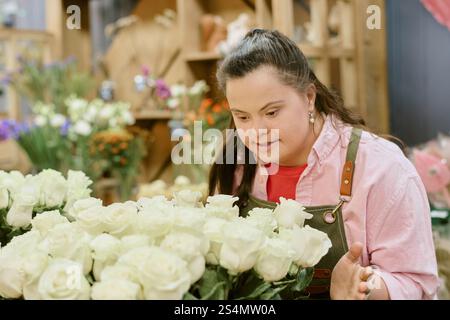 Primo piano medio di un giovane fioraio adulto che guarda le rose bianche della neve e l'aroma profumato Foto Stock