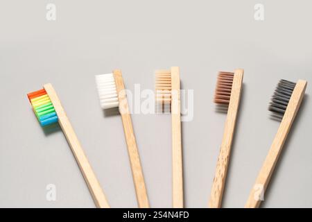 Varietà di spazzolini in bambù colorati e naturali con setole multicolore su sfondo grigio. Foto Stock