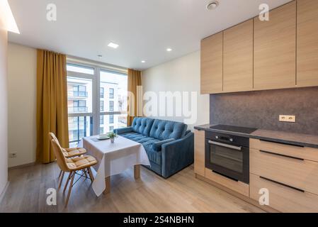 Interni luminosi e accoglienti con comodo divano, zona pranzo, cucina e grandi finestre. Moderno soggiorno dell'appartamento con cucina e Foto Stock