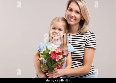 Donna felice con sua figlia e bouquet di fiori di alstroemeria su sfondo grigio. Festa della mamma Foto Stock