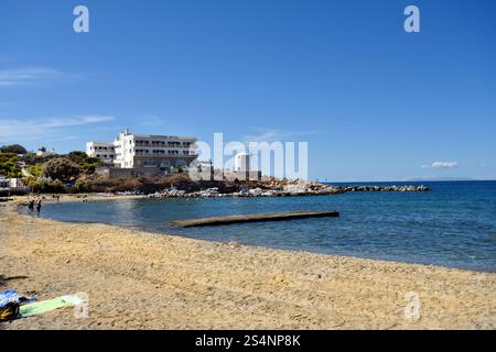 Paros, Grecia - 17 settembre 2024: Persone sconosciute sulla spiaggia di Parakia con un piccolo porto di pescatori e un mulino a vento che viene utilizzato come caffè Foto Stock