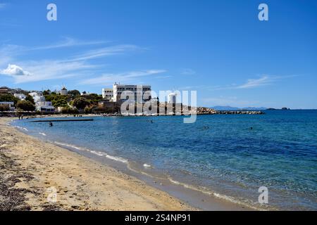 Paros, Grecia - 17 settembre 2024: Persone sconosciute sulla spiaggia di Parakia con un piccolo porto di pesca e mulini a vento, uno è usato come caffè Foto Stock