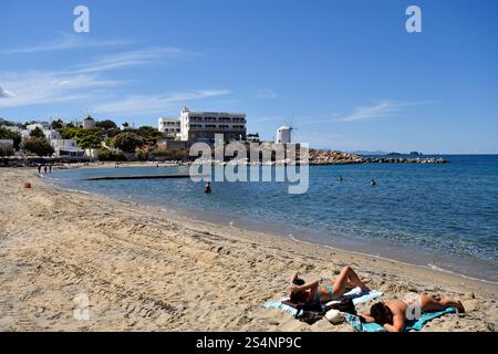 Paros, Grecia - 17 settembre 2024: Persone sconosciute sulla spiaggia di Parakia con un piccolo porto di pesca e mulini a vento, uno è usato come caffè Foto Stock