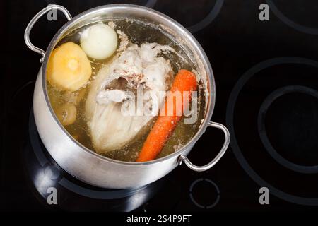 bollitura della zuppa di pollo con verdure aromatizzate in una padella di acciaio su una pentola in ceramica di vetro Foto Stock