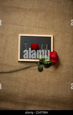 Red Rose e anello di nozze giacente sulla dichiarazione di amore scritte sulla lavagna Foto Stock