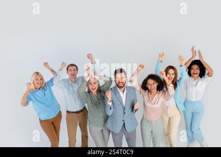 Gruppo eterogeneo di professionisti che celebrano insieme il successo su uno sfondo grigio chiaro, raffigurando il lavoro di squadra e la collaborazione. Foto Stock