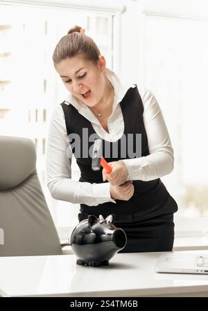 Ritratto di angry imprenditrice rompendo salvadanaio con martello Foto Stock