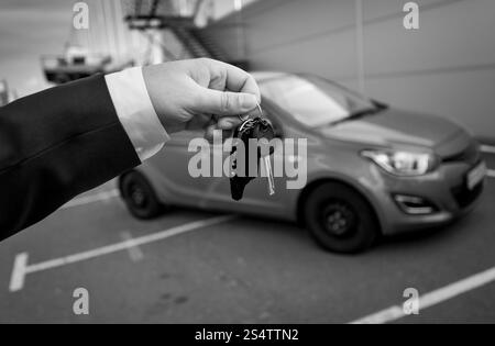 Primo piano in bianco e nero foto di un uomo vestito in azienda le chiavi dell'auto contro la nuova vettura Foto Stock