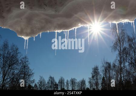 Sciogliendo i ghiaccioli con il cielo blu e il paesaggio naturale sullo sfondo. Clima primaverile con ghiaccio scongelato Foto Stock