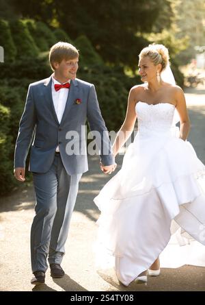 Bella sposa e sposo che si tengono per mano mentre cammina nel parco Foto Stock