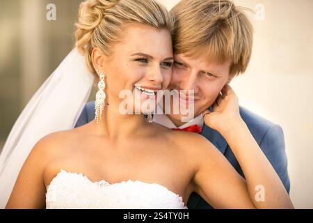 Ritratto ravvicinato della sposa sorridente e dello sposo che abbracciano la strada nelle giornate di sole Foto Stock