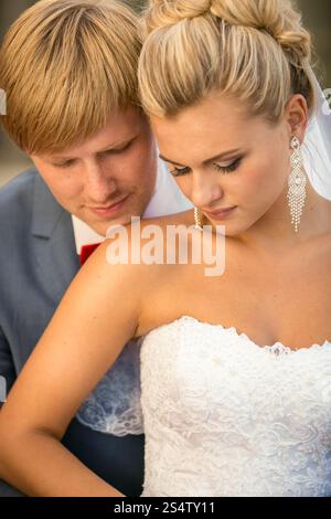 Ritratto ravvicinato di uno sposo giovane e bello che bacia la sposa bionda sulla spalla Foto Stock