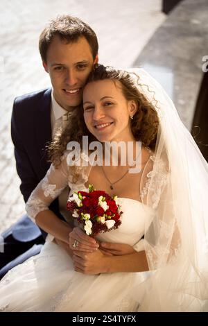 Bellissimo giovane sposo che abbraccia la sposa sorridente da dietro per strada Foto Stock