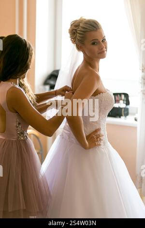 Ritratto di madre che assiste la sposa a indossare l'abito da sposa Foto Stock