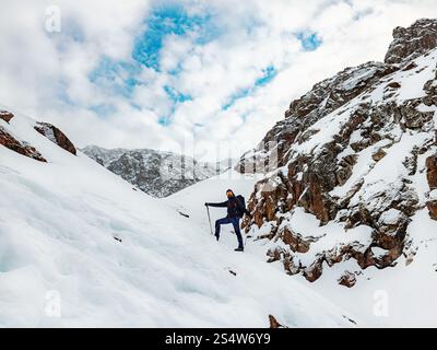 Un escursionista maschile in cima alle montagne in inverno. Viaggiatore barbuto con uno zaino in piedi su una pista innevata. Escursioni sulle montagne invernali Foto Stock