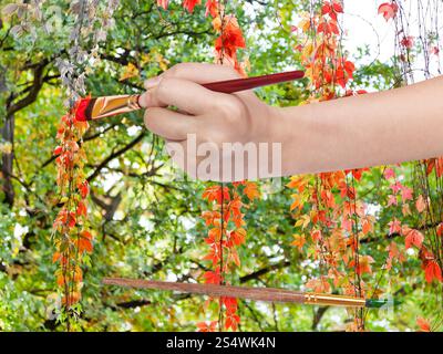 Concetto di natura - mano con pennello vernici rosse foglie della pianta rampicante in autunno Foto Stock