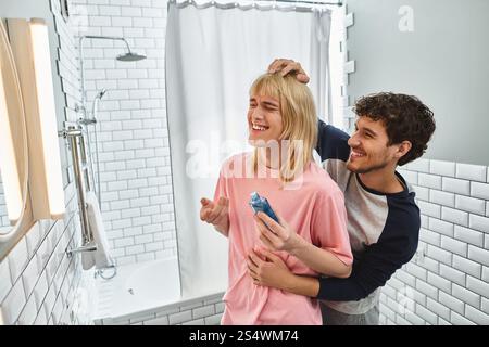 Due uomini si godono un momento di gioco mentre uno acconcia i capelli degli altri con risate in un bagno elegante. Foto Stock