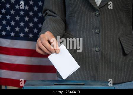 Mano che colloca il voto in una casella elettorale con la bandiera degli Stati Uniti nel concetto di elezioni in background Foto Stock