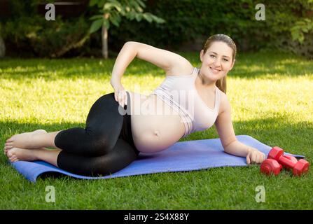 Felice la donna incinta che esercitano sul tappetino fitness presso il park Foto Stock