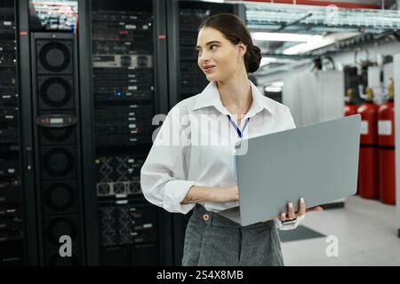 Una donna sicura di sé con una camicia bianca si impegna con il suo notebook in una sala server all'avanguardia. Foto Stock