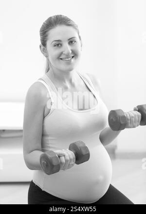 Ritratto in bianco e nero di sorridere donna incinta esercizio con manubri Foto Stock