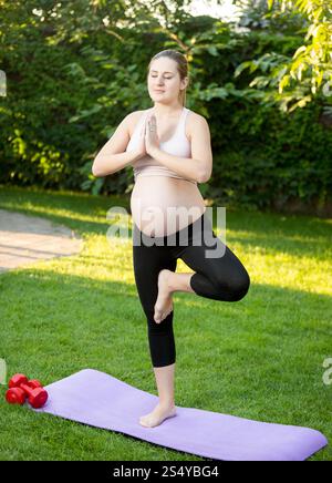 Giovane donna incinta che fa esercizio di yoga sull'erba Foto Stock