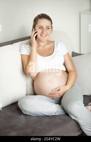Bella donna incinta sorridente che parla al telefono sul divano Foto Stock