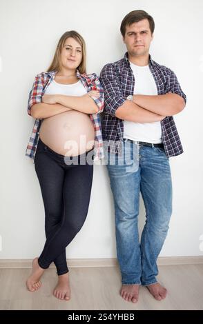 Felice coppia sorridente in attesa del bambino che posa in jeans e camicie Foto Stock