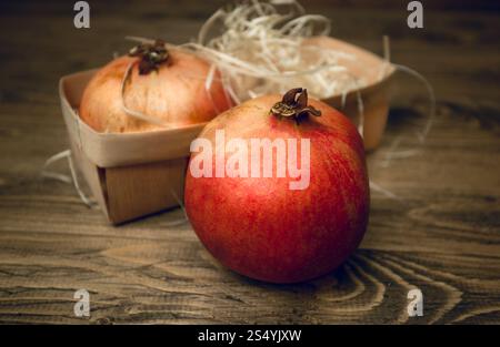 Primo piano di due melograni stesi nel cesto su una vecchia scrivania di legno Foto Stock