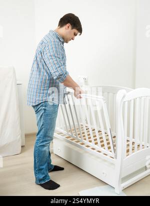 Bell'uomo in jeans e camicia che assembla un lettino per bambini Foto Stock