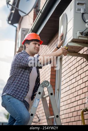 Tecnico maschio che ripara l'impianto di climatizzazione esterno Foto Stock