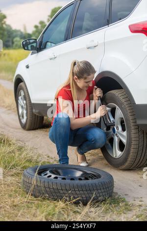 Donna che svita i dadi sulla ruota piatta dell'auto sul campo Foto Stock