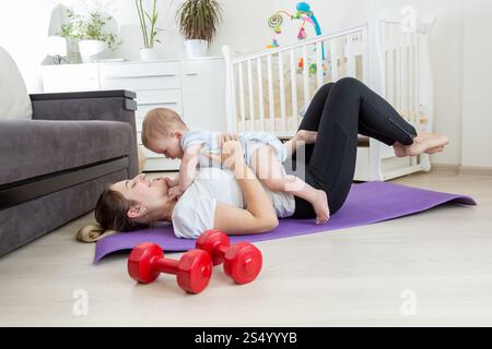Madre felice che fa esercizio fisico a casa e si diverte con il suo bambino Foto Stock