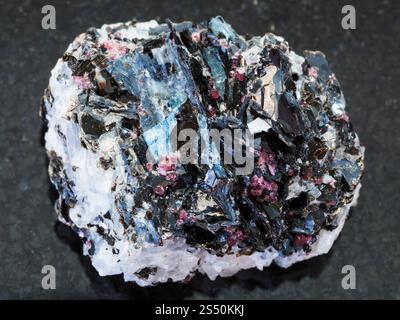 Riprese macro di un campione di roccia minerale naturale - pietra grezza di Gneiss con cristalli di biotite, cianite, tormalina su sfondo di granito scuro da Foto Stock