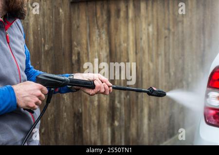 Foto ravvicinata di un uomo che lava la sua auto con una grande testa d'acqua di un karcher all'aria aperta. Pulizia e disinfezione. Le misure di sicurezza durano Foto Stock