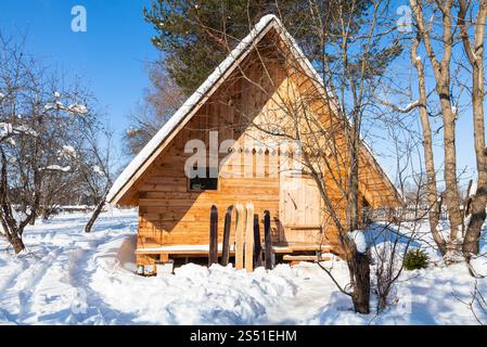 vista di un piccolo cottage in legno e di ampi sci. Vista di un piccolo cottage in legno e ampi sci nella soleggiata giornata invernale nella regione russa di Smolensk Foto Stock