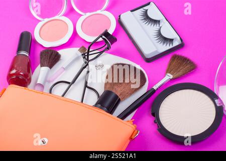 Vista dall'alto di una borsa per il trucco, con prodotti cosmetici che fuoriescono su uno sfondo rosa. Vista dall'alto di una borsa per il trucco, con bellezza estetica Foto Stock