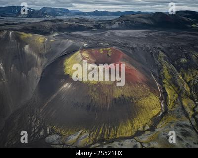 Vista aerea di un colorato cratere vulcanico nelle Highlands islandesi, caratterizzato da vibranti tonalità gialle e rosse circondate da un suggestivo terreno vulcanico. Foto Stock