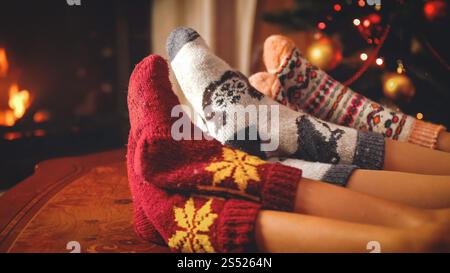 Immagine tonificata della famiglia in calze di lana adagiate accanto al camino in fiamme nel soggiorno. Foto tonificata di famiglia in calze di lana adagiate accanto al fuoco Foto Stock