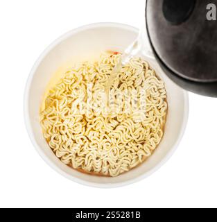 La cottura di tagliatelle istante - versare acqua dal bollitore nella tazza con secchi tagliatelle istante isolato su sfondo bianco Foto Stock