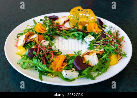 Un'insalata vivace presenta rucola fresca, barbabietole colorate, formaggio e decorazioni splendidamente disposte. Questo piatto presenta una presentazione artistica ideale Foto Stock