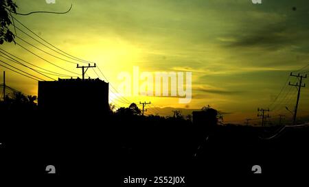 Una splendida silhouette al tramonto con linee elettriche ed edifici su un cielo giallo e verde vibrante. La scena cattura la tranquillità del crepuscolo in una u Foto Stock